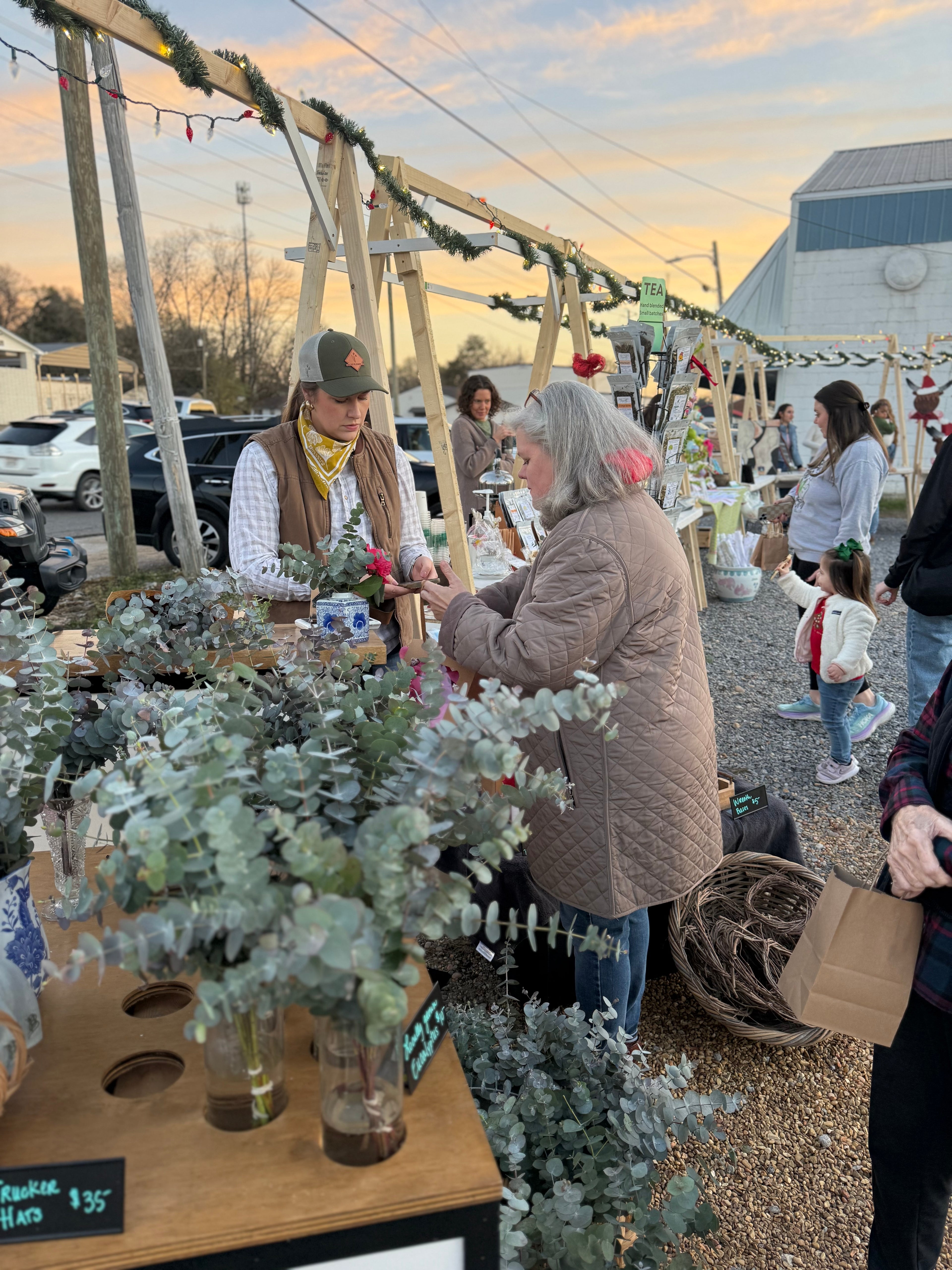 Hannah arranges flowers at an outdoor market stall with other people in the background.